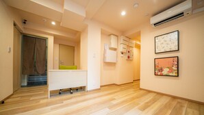 A spacious room with wooden flooring, a white desk, a green chair, and a bathroom with a shower and toilet.