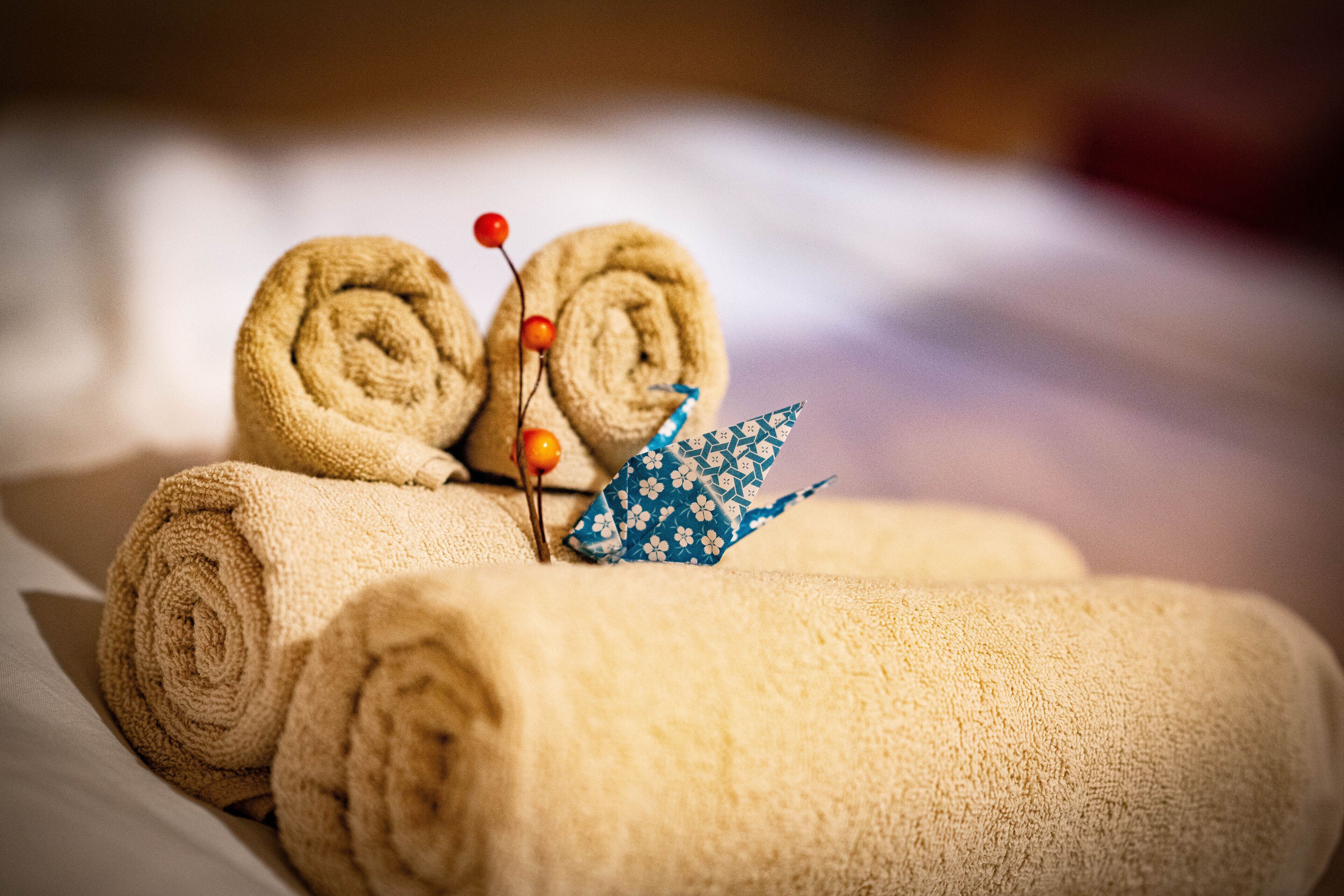 Neatly rolled towels and a decorative blue paper crane on a bed.