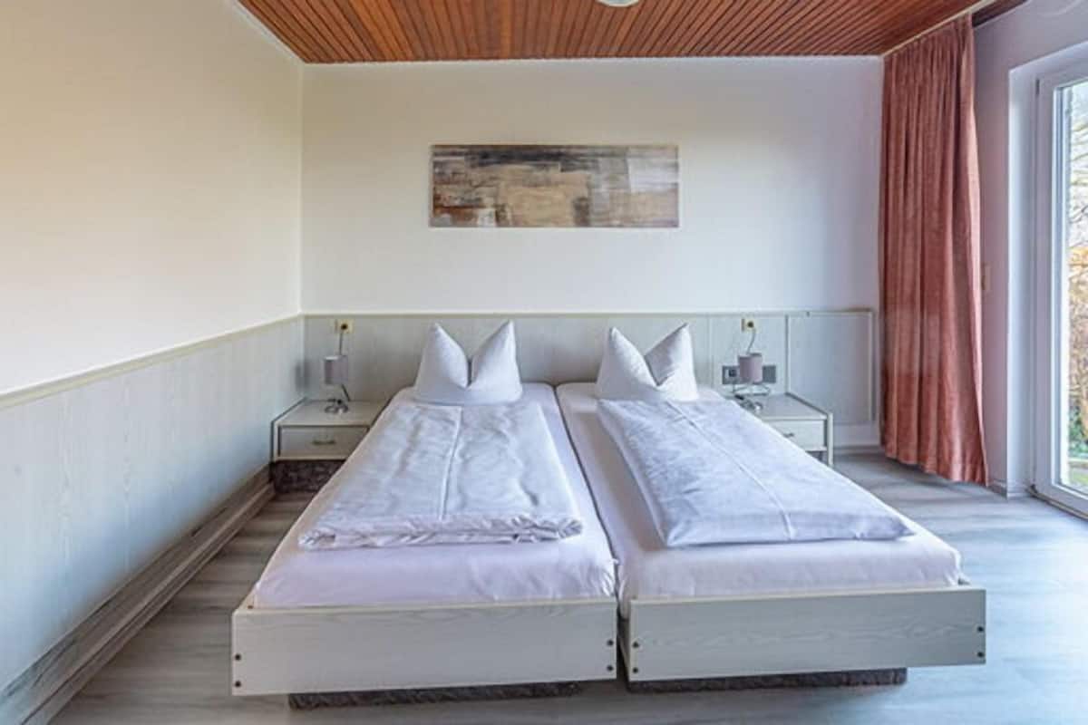 A double bed with a wooden headboard and two bedside tables, one with a lamp.