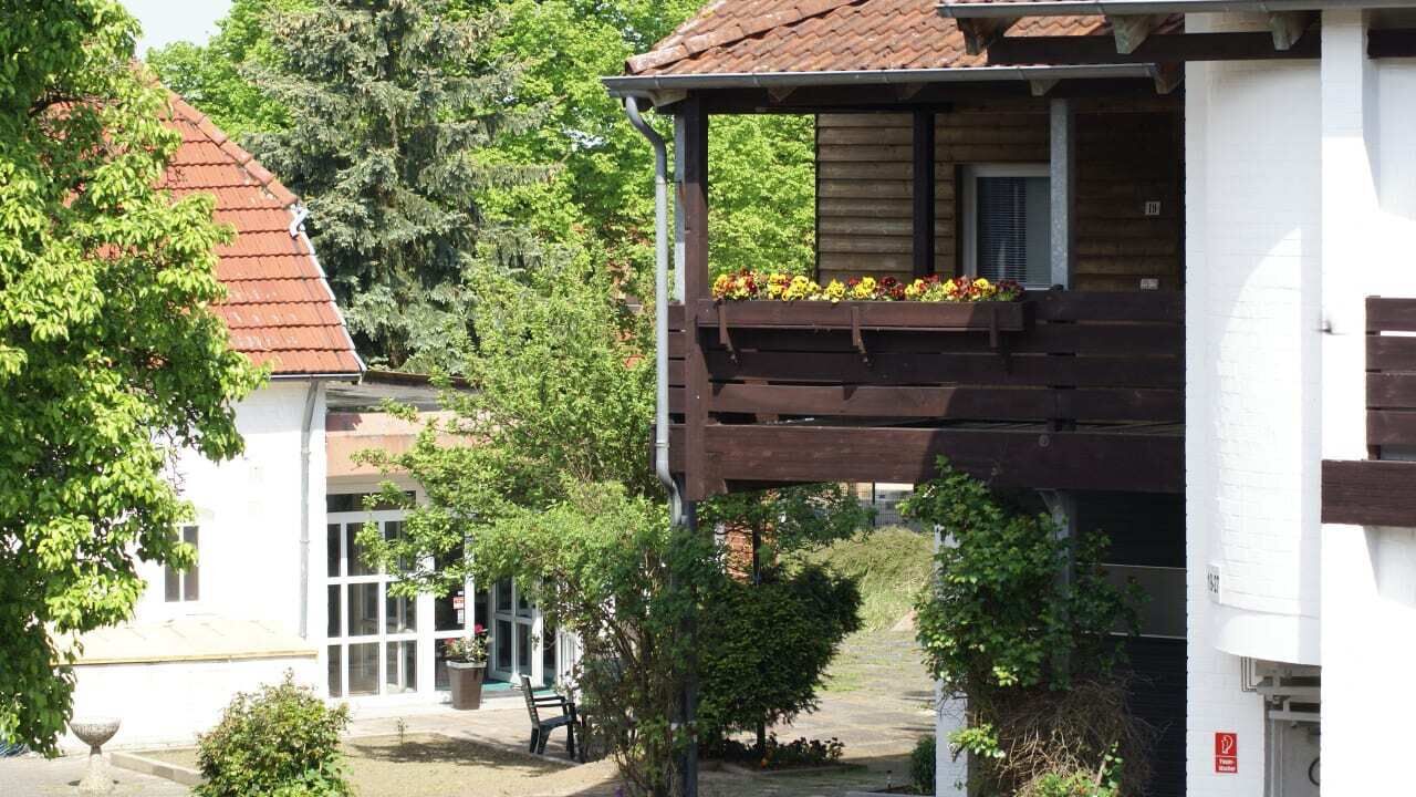 A building with a wooden balcony, a garden area, and a white facade.