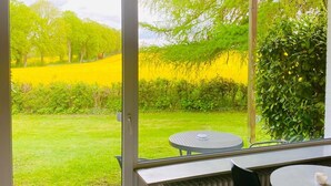 A room with a large sliding glass door leading to a garden. Inside, there is a round table with a chair and a radiator. - K357 - Monteurhotel Ostsee Lounge (Ratekau)