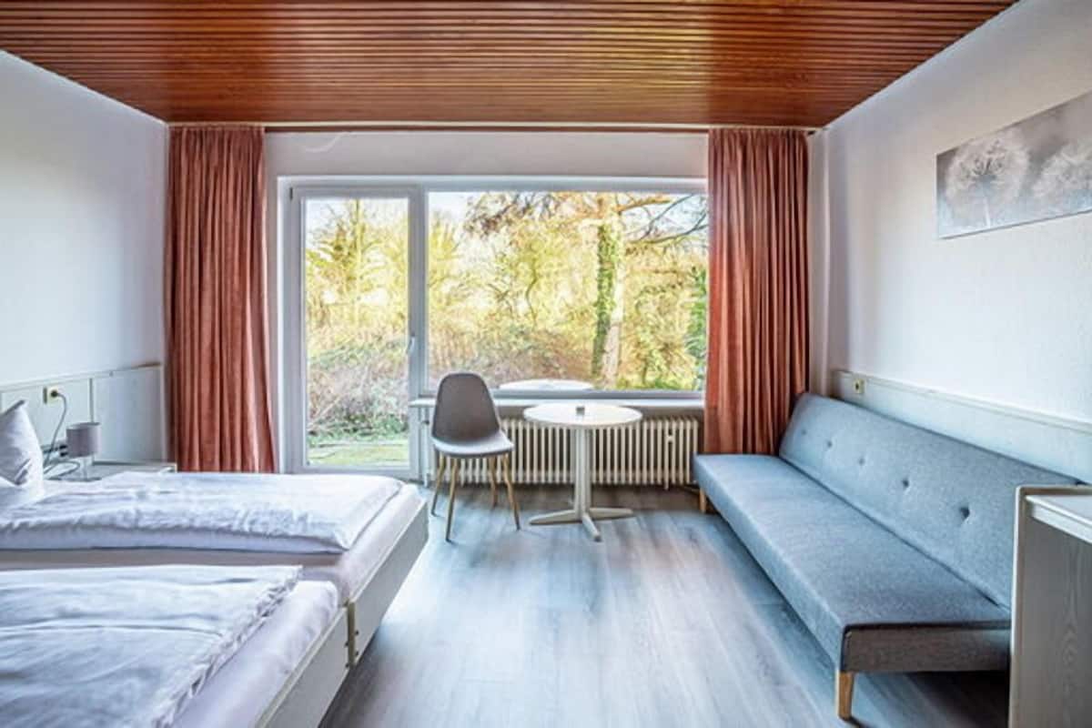 A modern hotel room with a large window, a round table, and a sofa.
