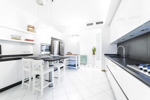 Cozinha moderna com armários brancos, bancada preta e um espaço de jantar com cadeiras brancas.