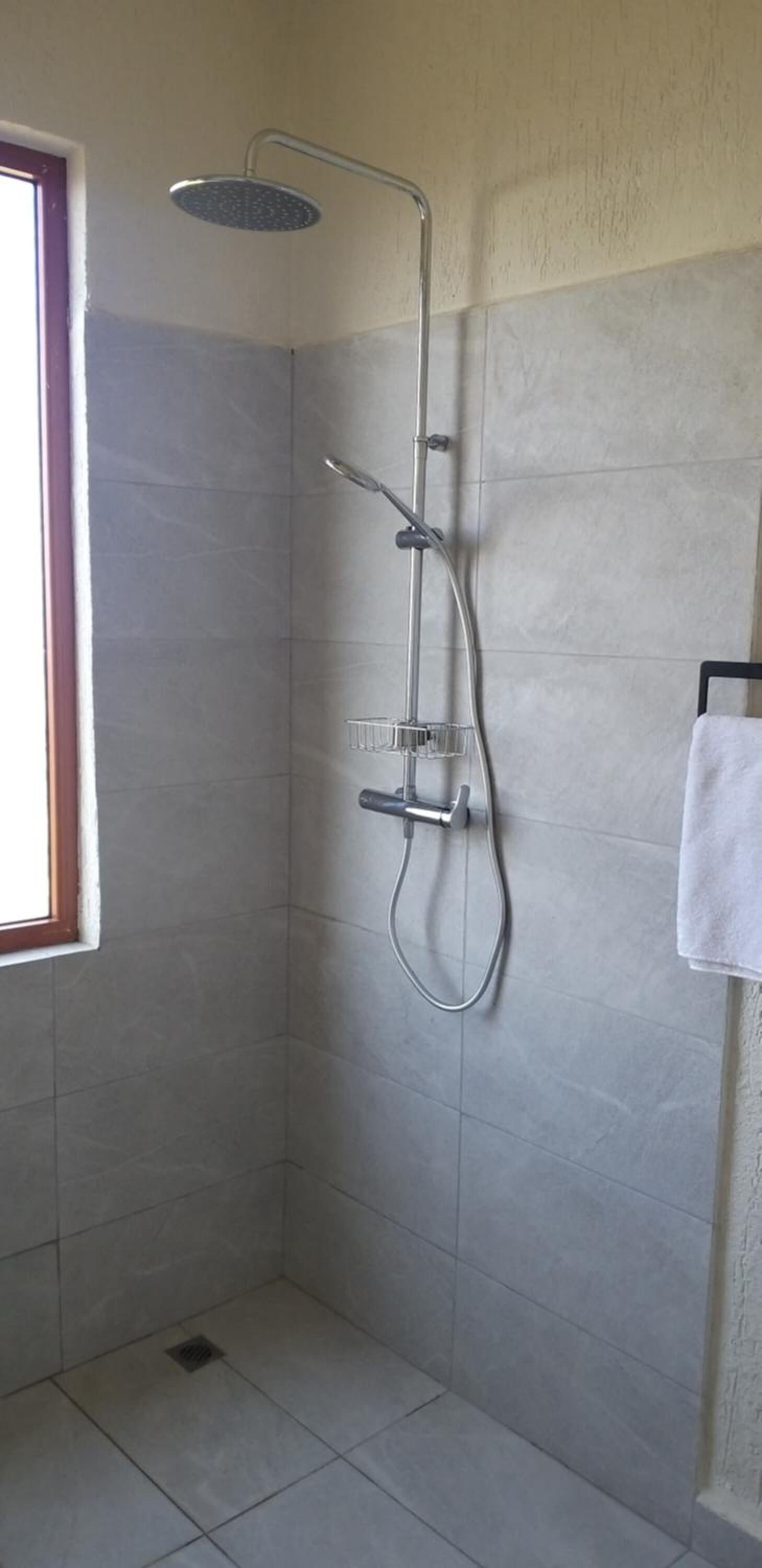 A shower with a handheld showerhead and a wall-mounted faucet, tiled walls, and a window.