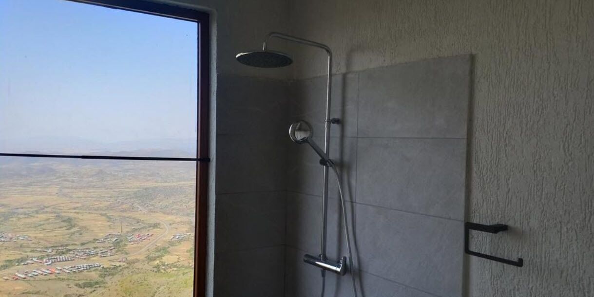 Une salle de bain avec douche, une vue sur un paysage à travers une grande fenêtre et un mur carrelé.