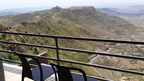 Un balcón con vistas a un paisaje montañoso, que incluye campos en terrazas y un camino sinuoso.