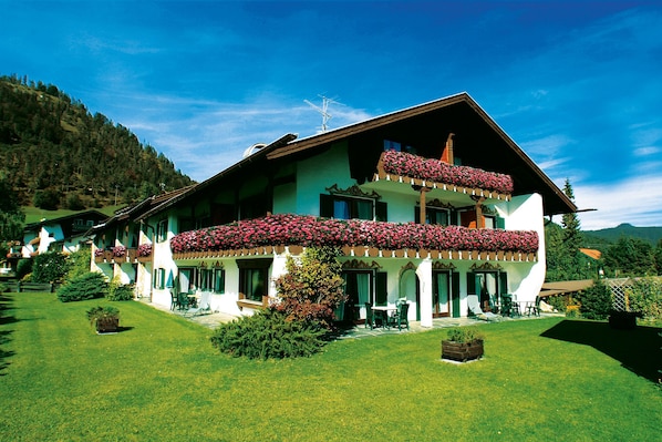 Ein großes, zweistöckiges Chalet mit Blumen geschmücktem Balkon, umgeben von einem gepflegten Rasen und einer Bergkulisse.
