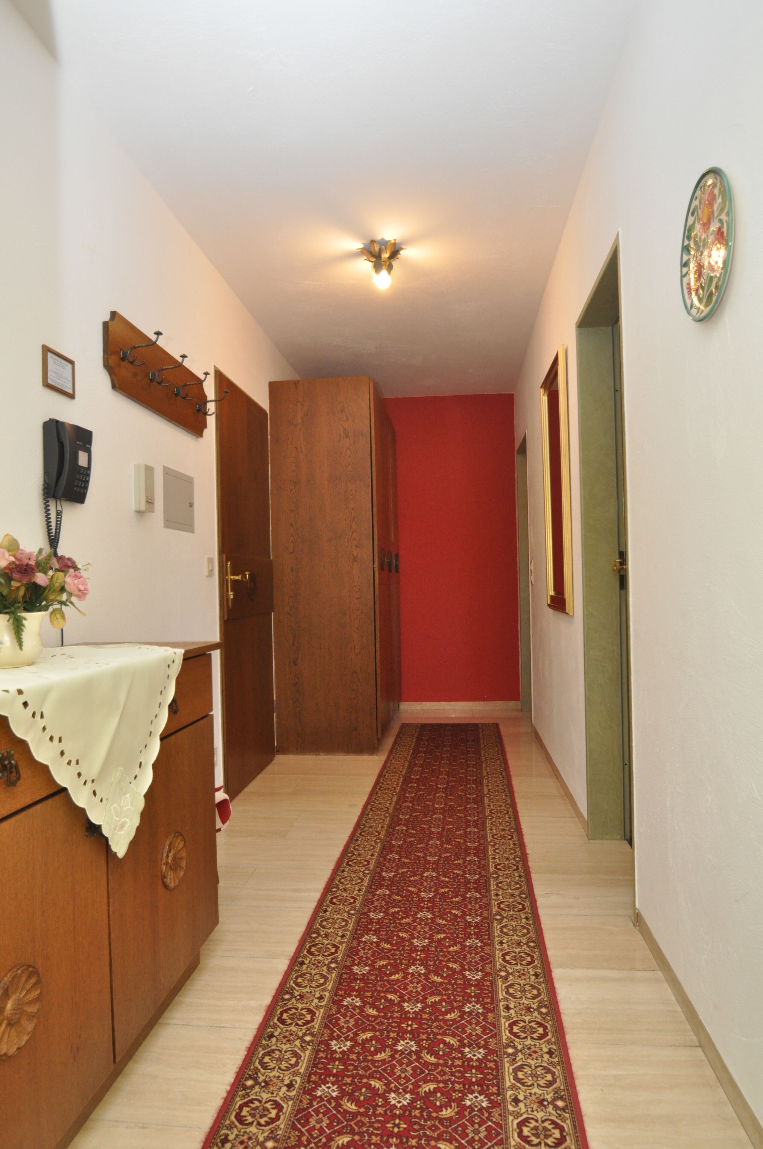 Un couloir avec un tapis rouge, des meubles en bois, un téléphone et un luminaire fixé au mur.