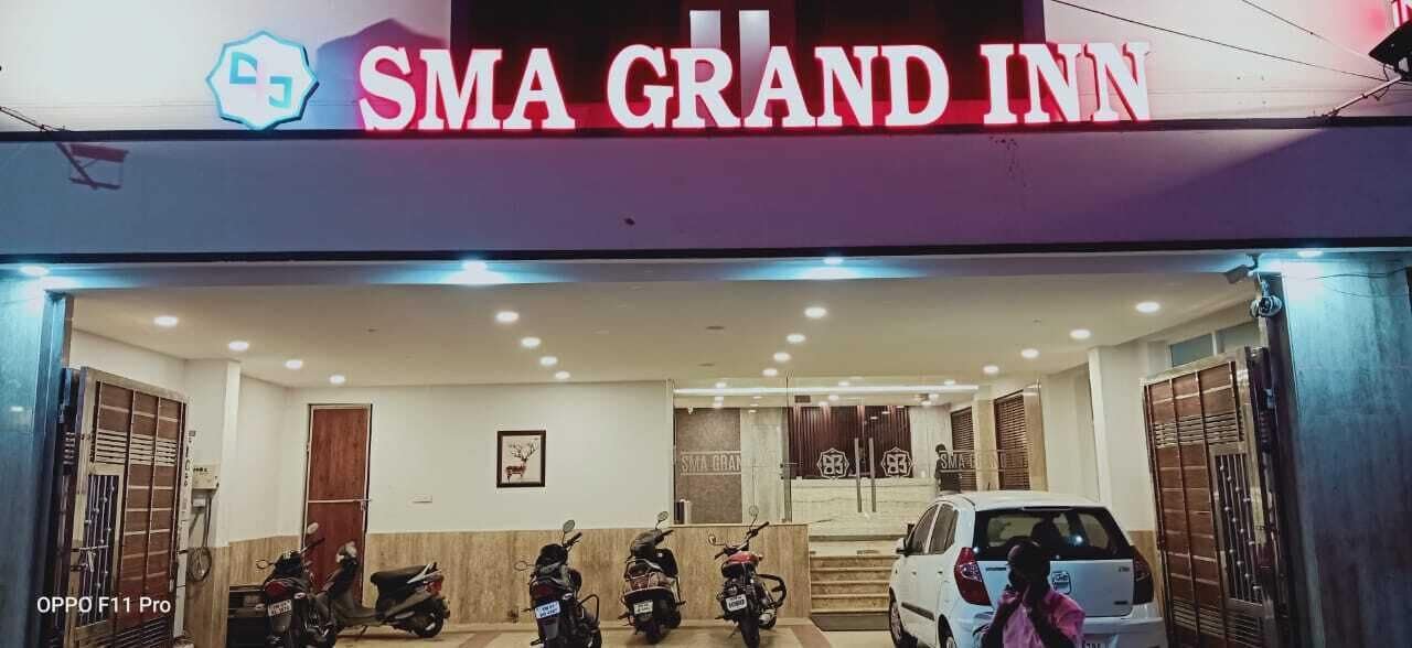 The entrance of SMA Grand Inn with a sign, a staircase, and parked vehicles.