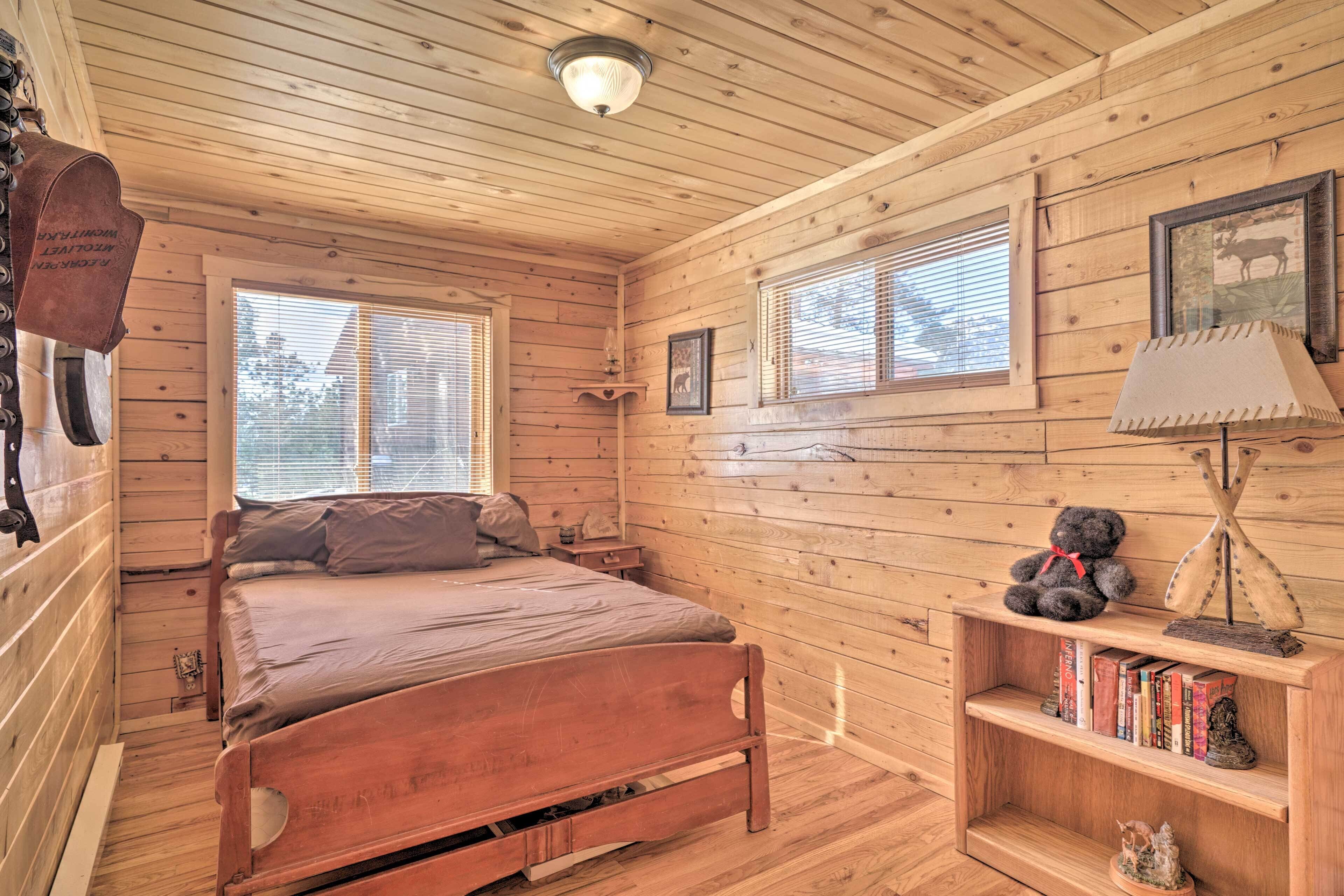 A wooden cabin bedroom with a bed, a shelf with books and a teddy bear, and a mounted animal head.