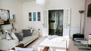 Een moderne woonkamer met een bank, een glazen salontafel, een bed en een eethoek met een tafel en stoelen.