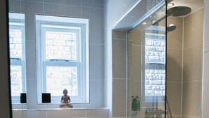 Een moderne badkamer met een douchecabine van glas, een witte wastafel en een raam boven het toilet.