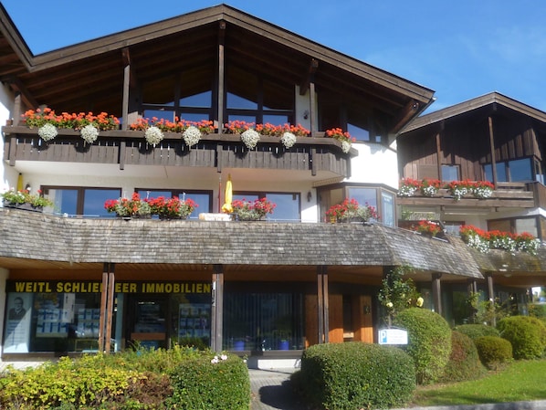 A hotel with a wooden facade, balconies with flower boxes, and a sign for 'WEITL SCHLIER IMMOBILIEN'.