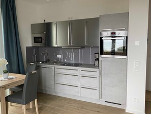 Uma cozinha compacta com micro-ondas embutido, eletrodomésticos de aço inoxidável, pia e área de refeições com mesa e cadeiras.