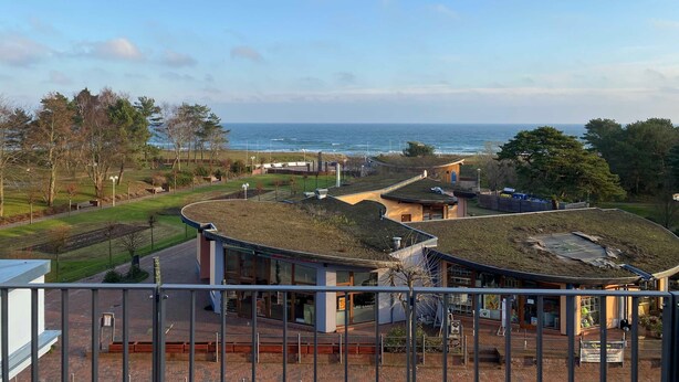 A coastal view with a building featuring a green roof, a paved walkway, and a view of the sea. - Baabe villas ensemble VE 19 sea view romanticism Ref. 215919 (Baabe)