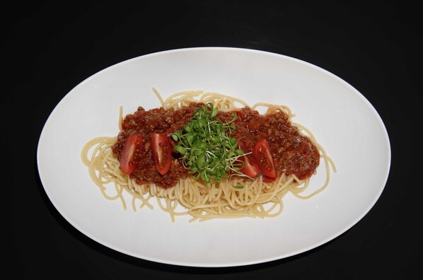 Un plato de espagueti con salsa de carne y rodajas de tomate.