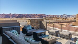 Una terraza en la azotea con mobiliario exterior, un muro de piedra y vistas a las montañas.
