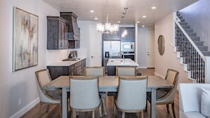 Una cocina moderna con una isla central, electrodomésticos de acero inoxidable y un comedor con mesa de madera y sillas tapizadas.