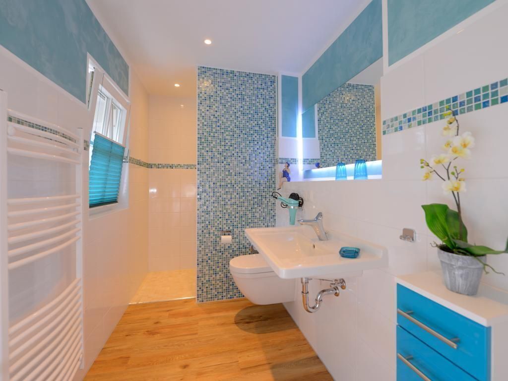 A modern bathroom with a shower, toilet, sink, and blue-tiled walls.