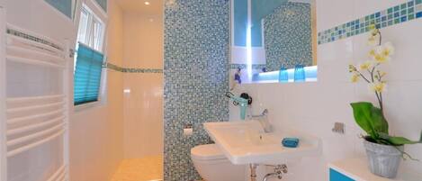 A modern bathroom with a shower, toilet, sink, and blue-tiled walls.