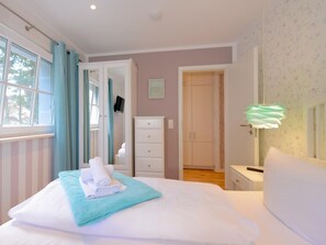 A bedroom with a bed, a dresser, a nightstand, and a window with curtains.