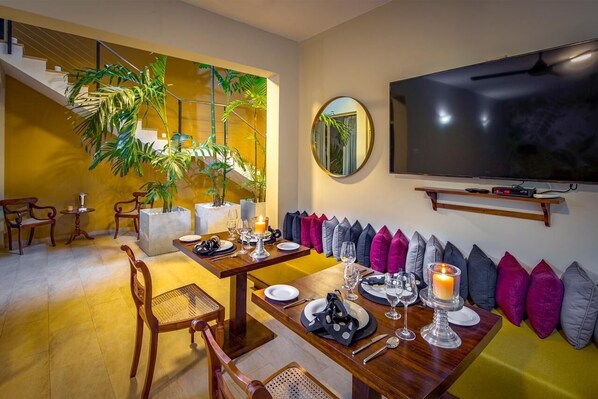 A dining area with a wooden table set for two, a large mirror, and a television mounted on the wall.