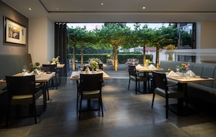 Un comedor interior con mesas y sillas, un sofá, y un ventanal con vistas a un jardín.