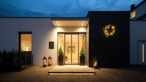 A modern hotel entrance with a glass door, potted plants, and a wreath decoration. - Hotel zur Post Riesenbeck (Hoerstel)