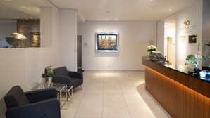 A modern reception area with a wooden reception desk, a glass coffee table, and two dark-colored sofas. - Hotel zur Post Riesenbeck (Hoerstel)