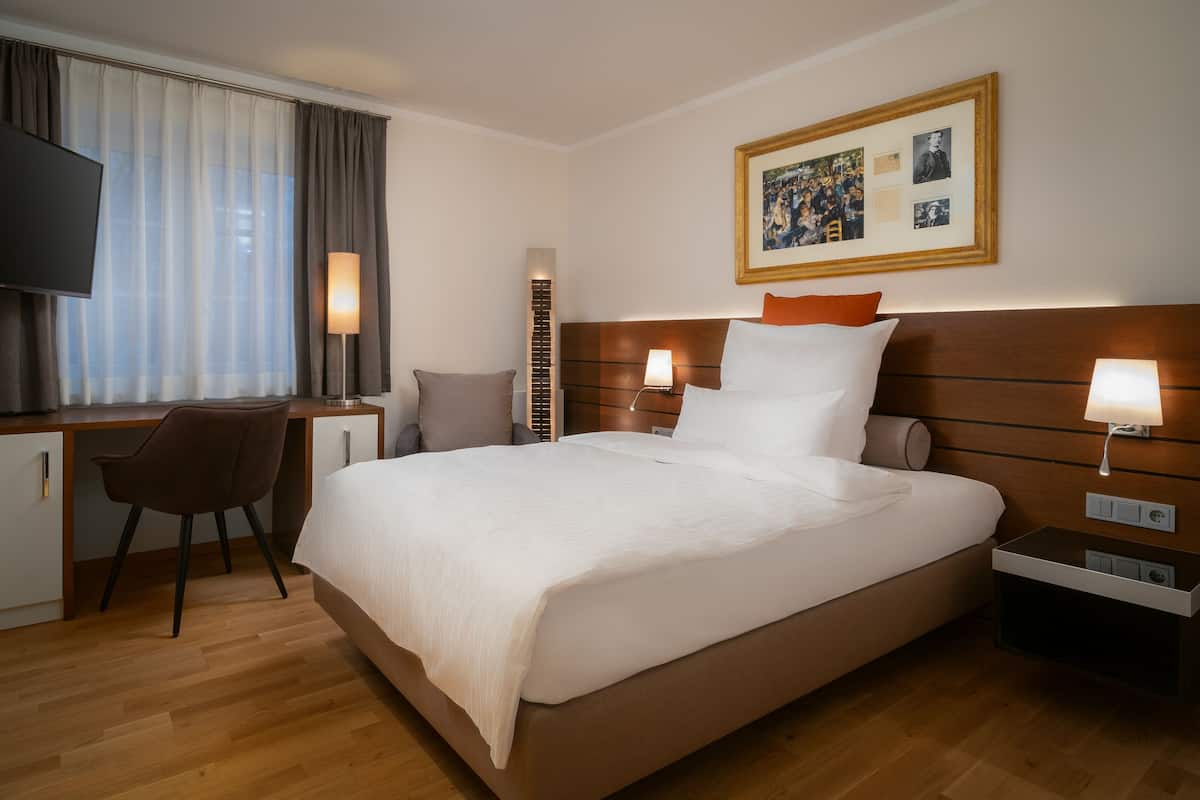 Quarto de hotel com uma cama grande, uma escrivaninha, uma cadeira e uma televisão.