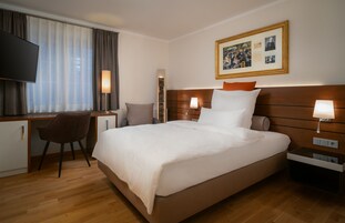 Habitación de hotel con una cama grande, un escritorio, una silla y un televisor.