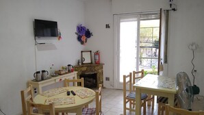 Zona pranzo con tavolo rotondo e sedie, televisione a parete, camino e finestra con vista esterna.