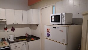 Una cucina compatta con mobili bianchi, un forno a microonde, un frigorifero e un lavello.