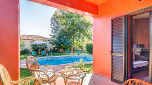 A pool area with wicker chairs, a glass table, and a sliding glass door leading to a room with a bed and a fireplace. - Peaceful two storey villa with traditional aesthetics (Heraklion)