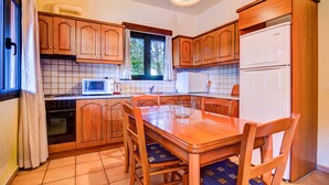 A compact kitchen with wooden cabinets, a microwave, a stove, and a refrigerator. - Peaceful two storey villa with traditional aesthetics (Heraklion)