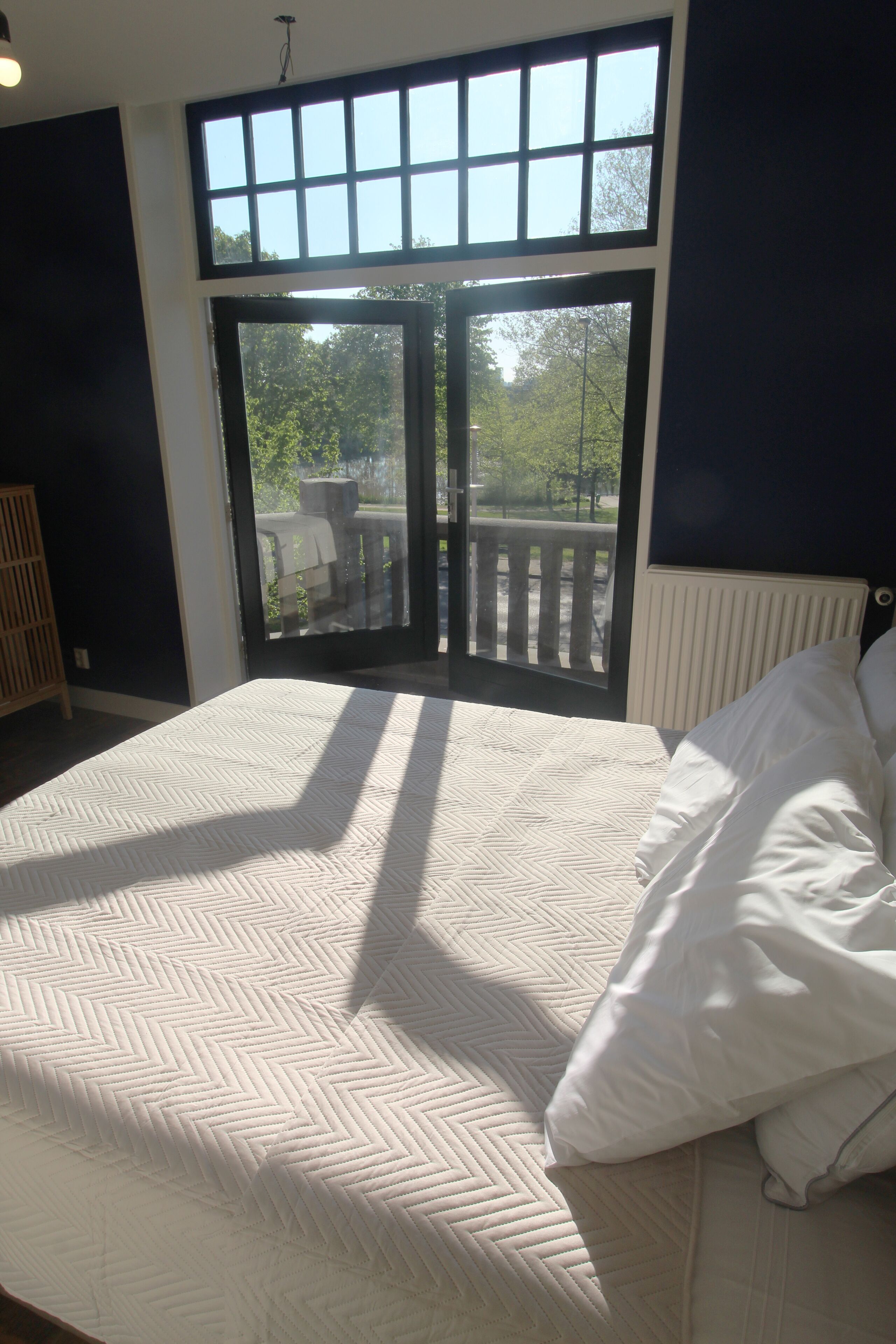 A bedroom with a large bed, a view through a sliding glass door, and a wooden deck outside.