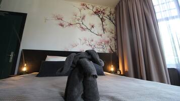 Une chambre d’hôtel avec un lit, un mur orné d’une fresque florale, une fenêtre avec des rideaux et une table de chevet avec une lampe.