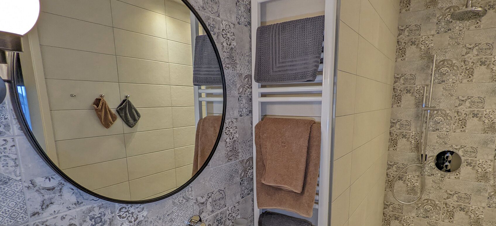 Een badkamer met een ronde spiegel, betegelde vloer, een handdoekrek en een douchecabine.