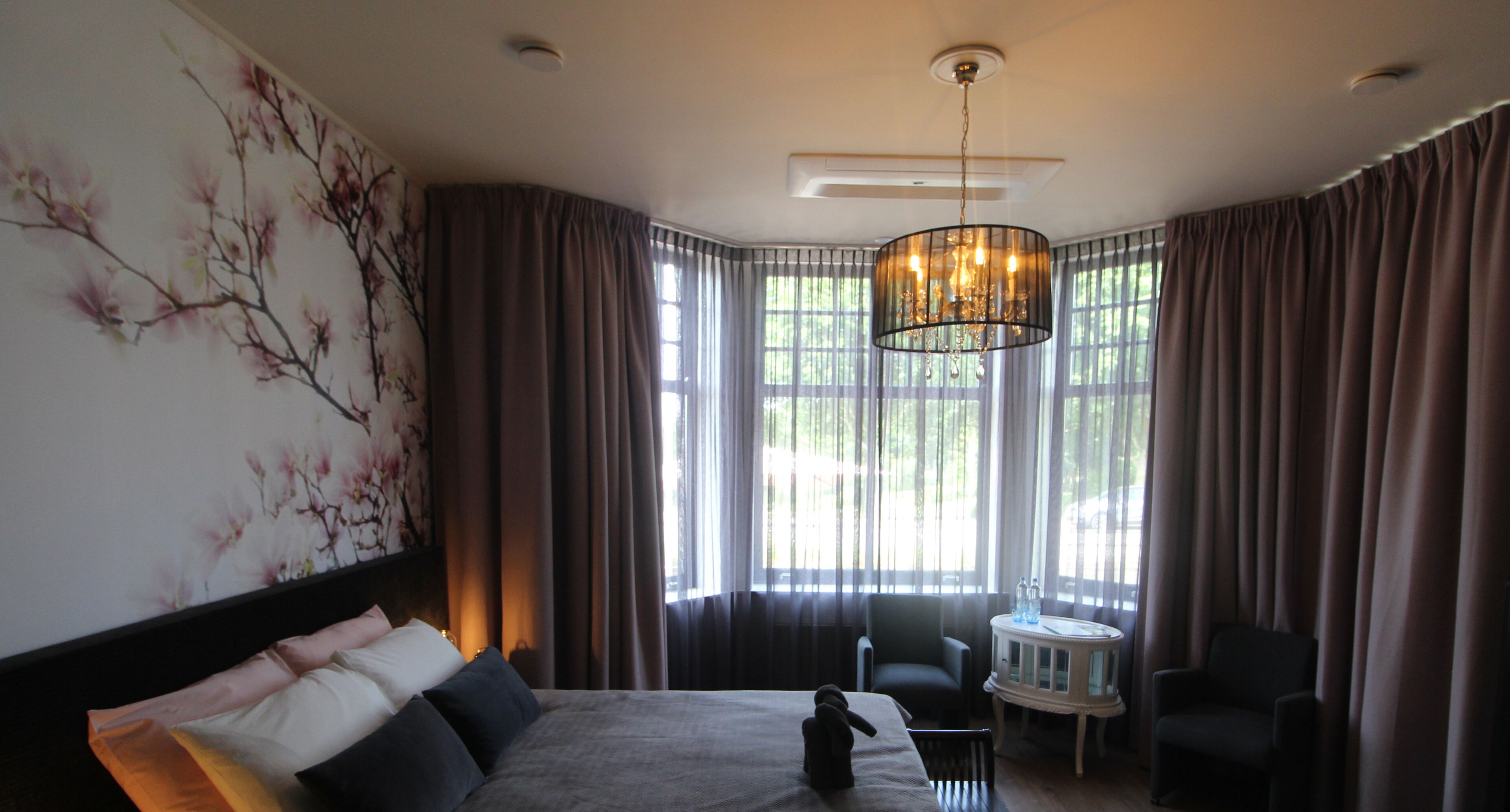 A hotel room with a large bed, a chair, a small table, and a chandelier.