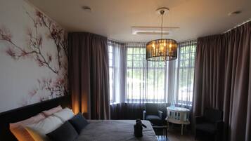 A hotel room with a large bed, a chair, a small table, and a chandelier.