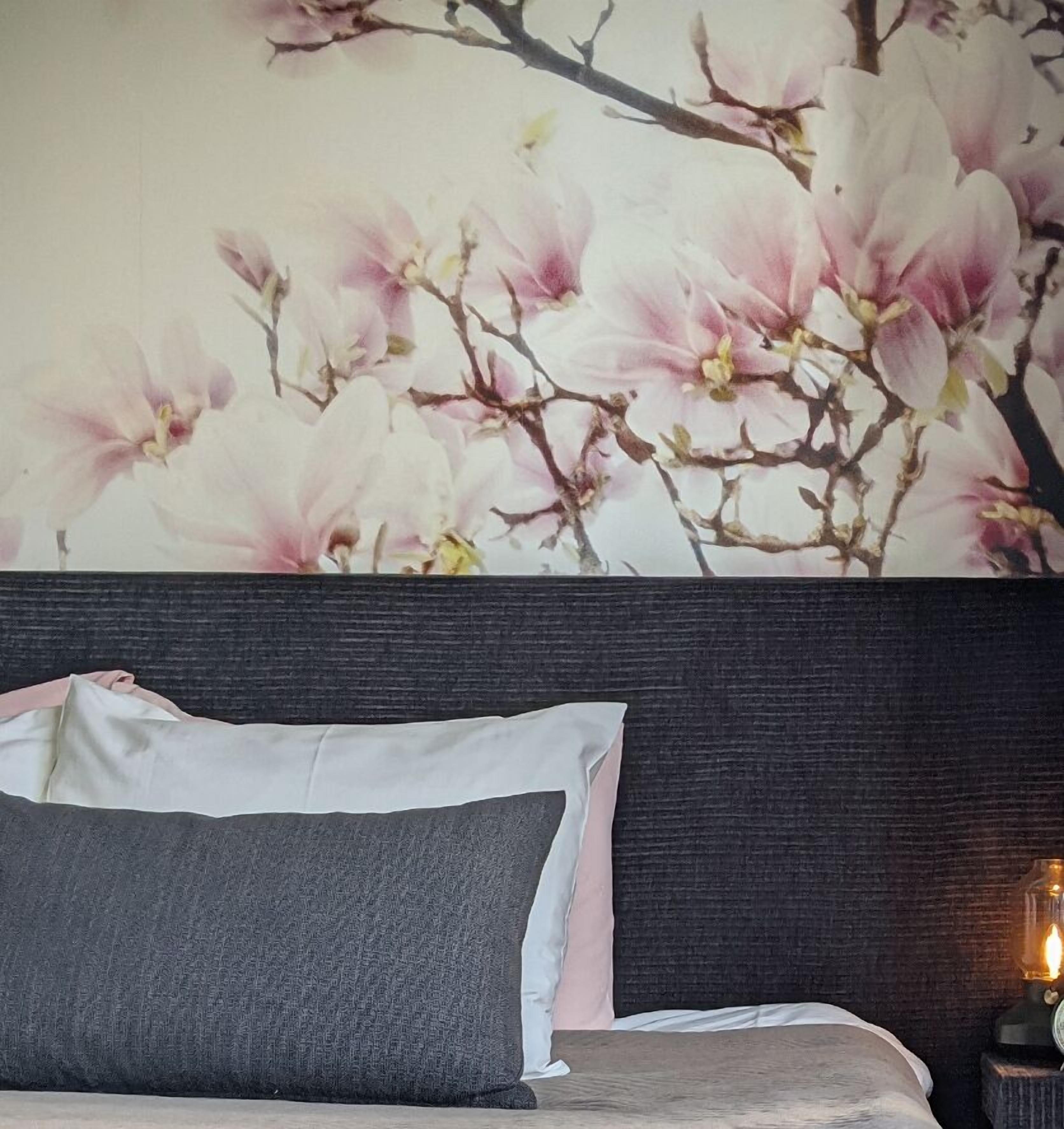 A bedroom with a large floral wall mural, a dark headboard, and a bedside lamp.