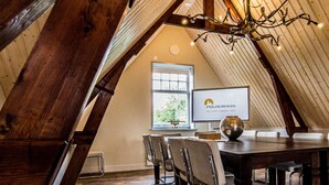 A dining area with a wooden table and chairs, a chandelier, and a window with a view of greenery. - Polderhuis Bed & Breakfast (Bergschenhoek)