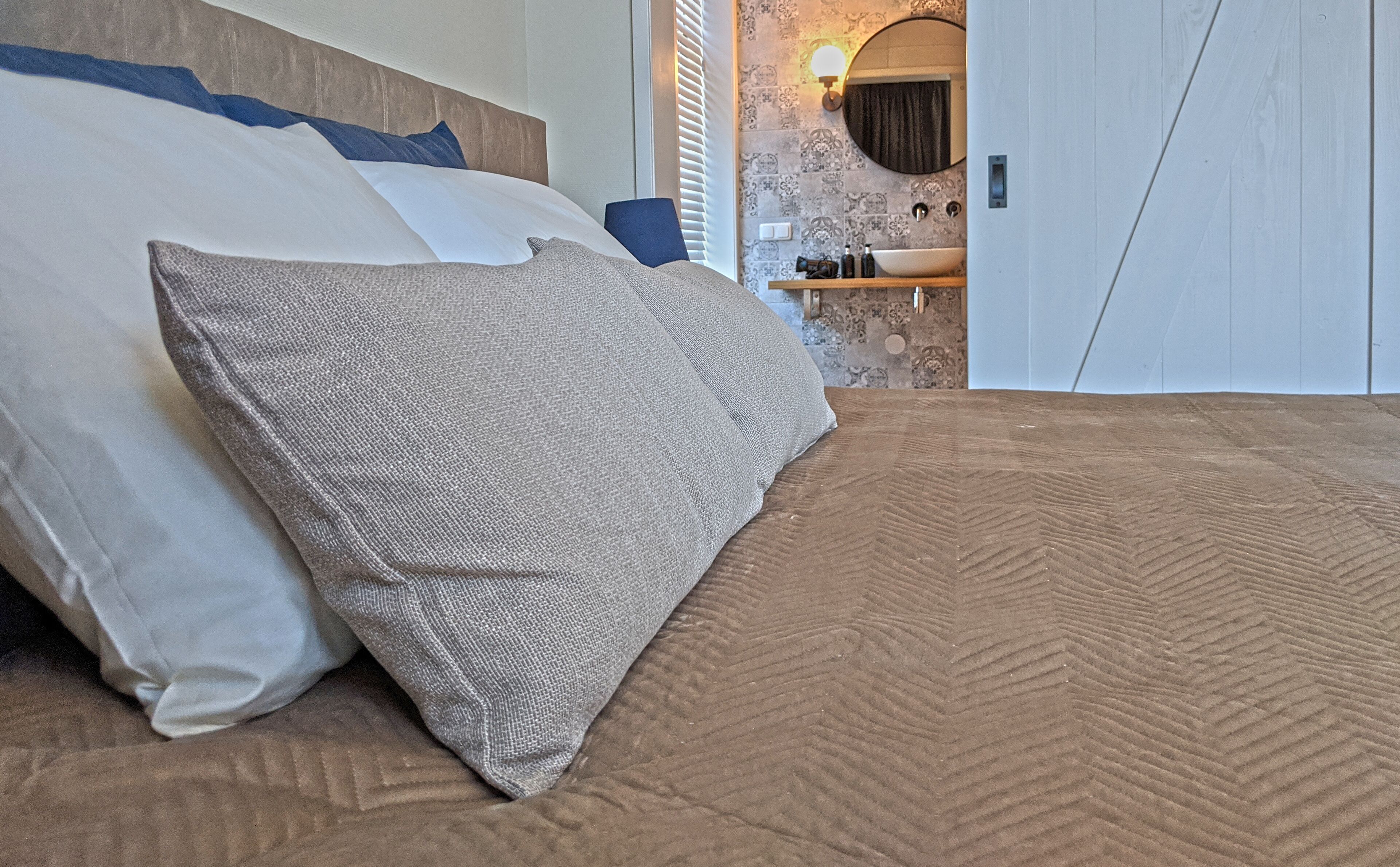 A bed with a textured brown cover and a grey pillow.