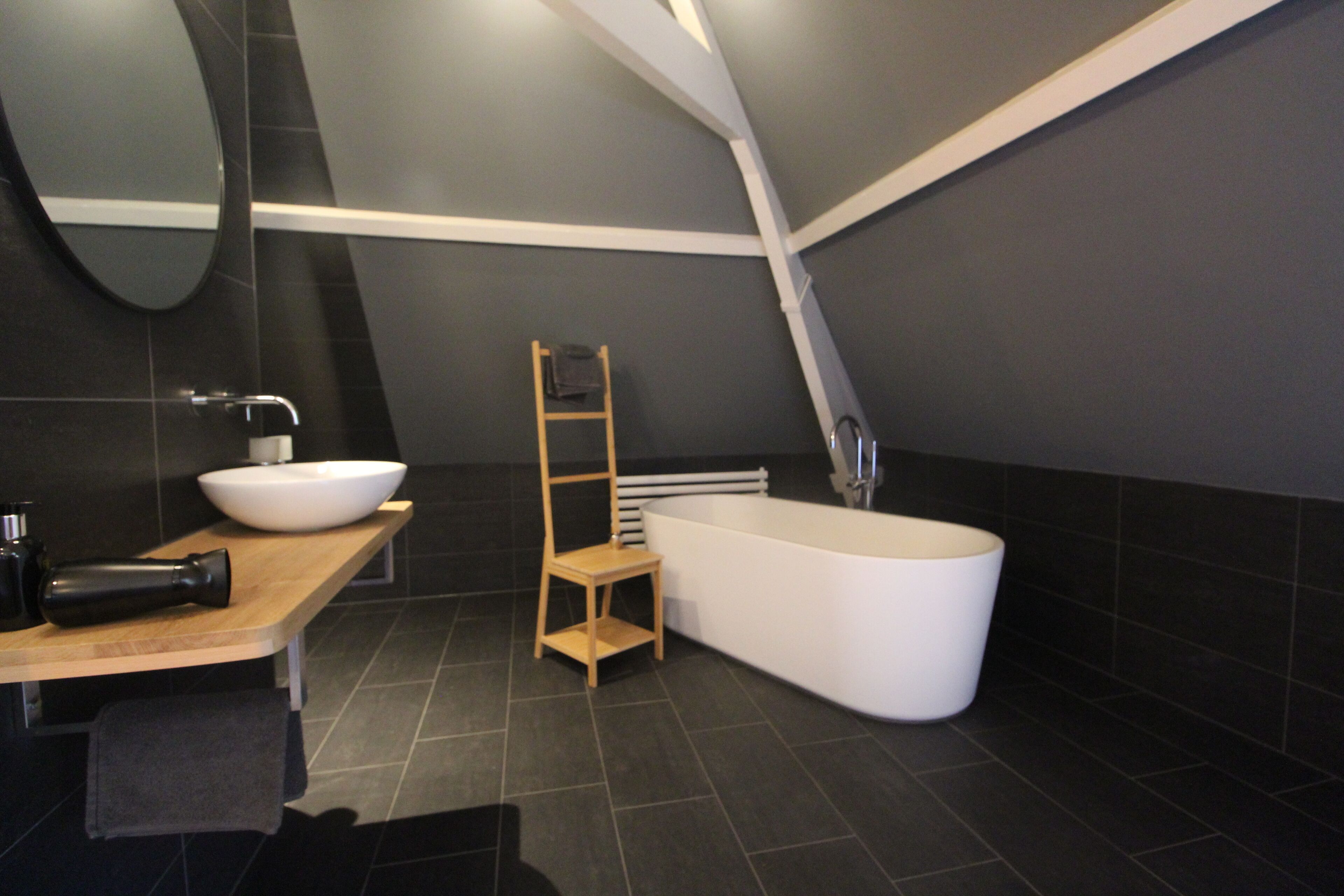 A modern bathroom with a freestanding bathtub, a wooden vanity, a mirror, and a towel rack.