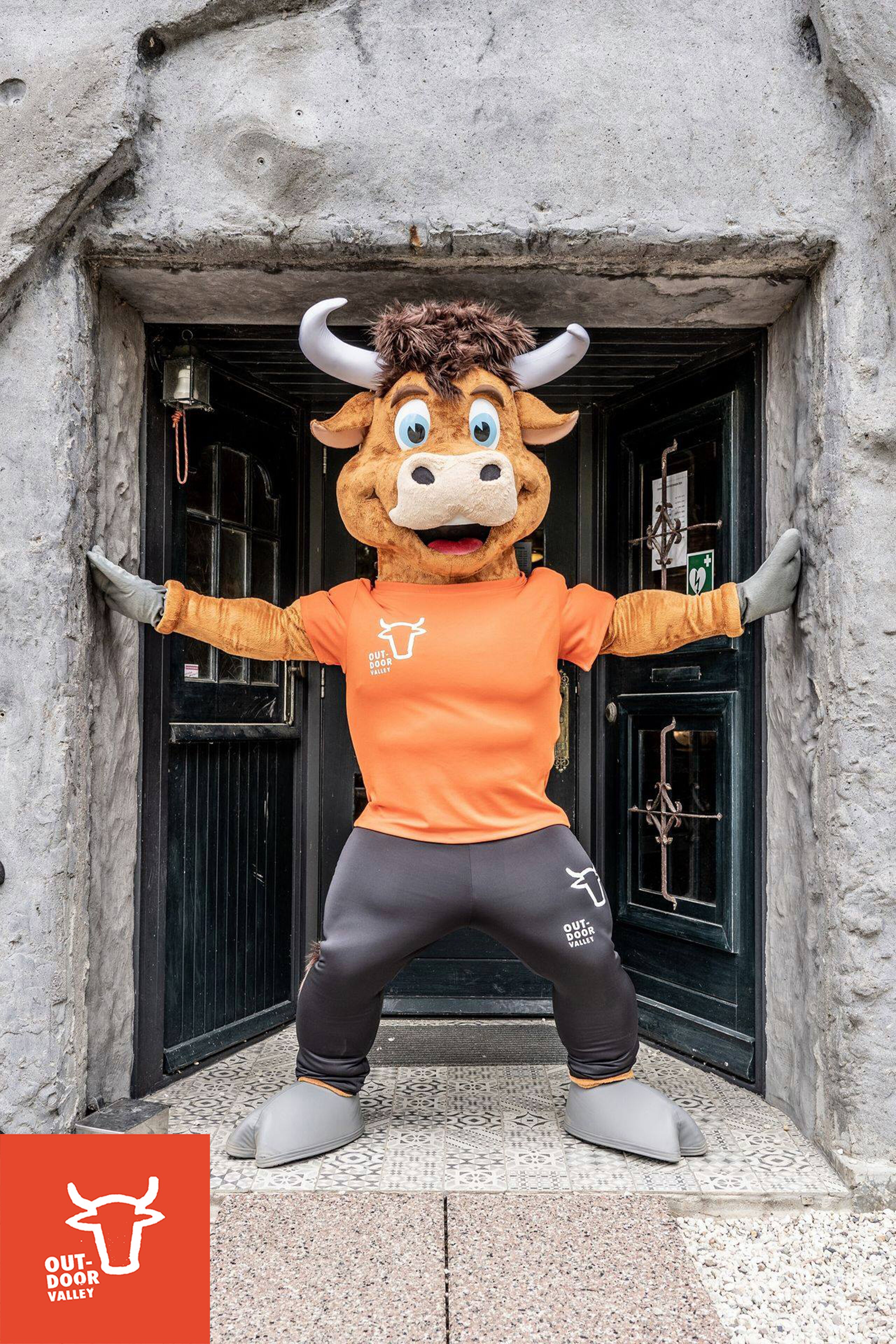 Une mascotte déguisée en taureau se tient devant l’entrée d’un bâtiment.
