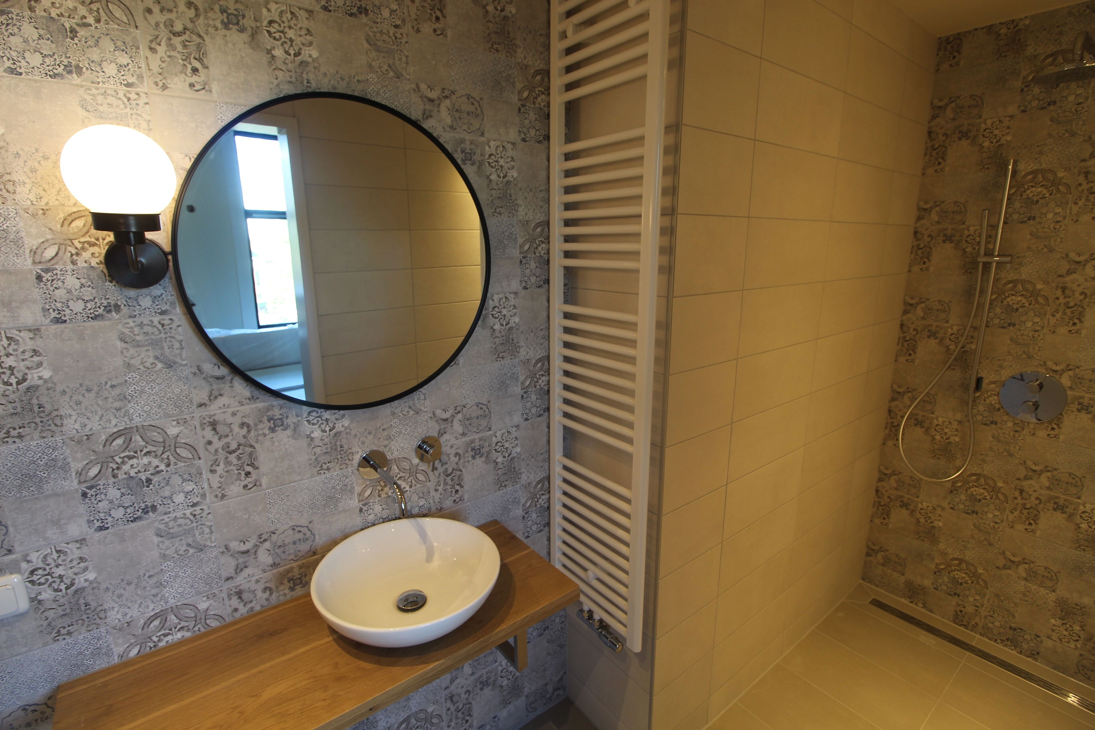 A bathroom with a round mirror, a wooden vanity, a white sink, and a shower with a glass door.