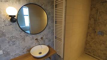 A bathroom with a round mirror, a wooden vanity, a white sink, and a shower with a glass door.