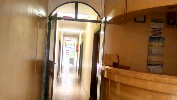 A hallway with a reception desk, a sign indicating 'ROOMS', and a bulletin board with posted notices. - Sundowner Lodge (Nakuru)