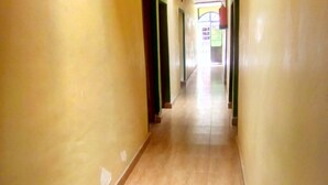 A narrow hallway with yellow walls and a wooden floor, leading to a brightly lit room with a green door. - Sundowner Lodge (Nakuru)