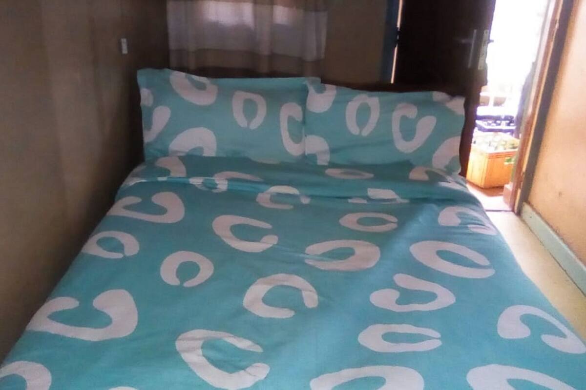 Una habitación pequeña y estrecha con una cama cubierta por una colcha de diseño azul turquesa y blanco.